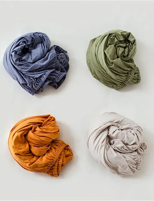 Four crumpled fabric swatches in blue, green, orange, and beige on a white background