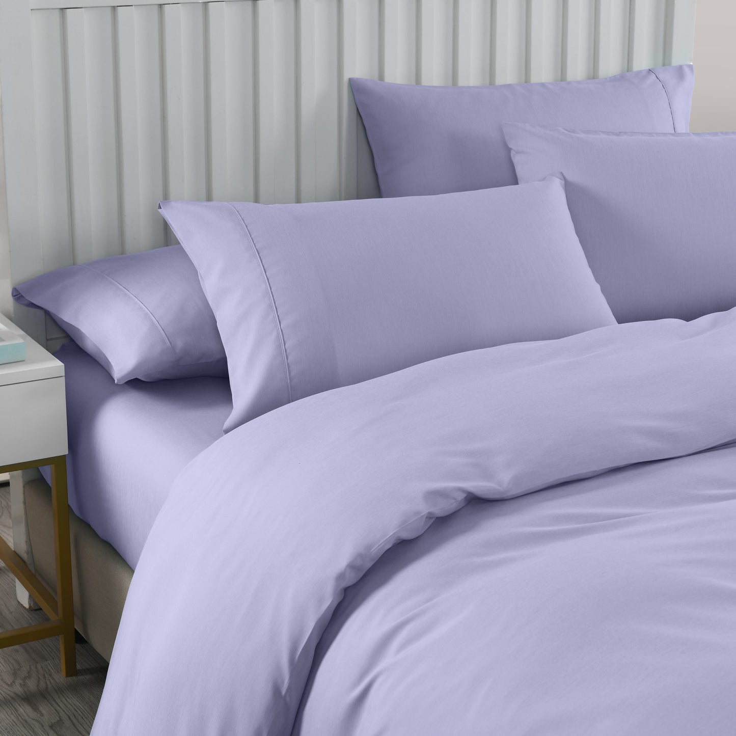 Lilac bedding set on a bed with a neutral headboard and nightstand.