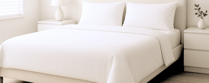 Neatly made bed with white dust mite bedding protectors and pillows in a bedroom setting.