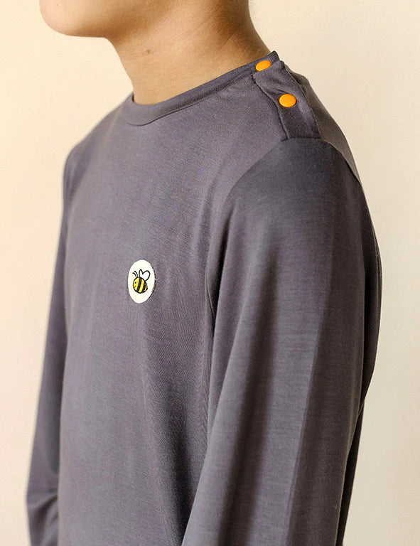 Close-up of orange shoulder snap buttons and bee logo on a dark gray organic bamboo pyjama top