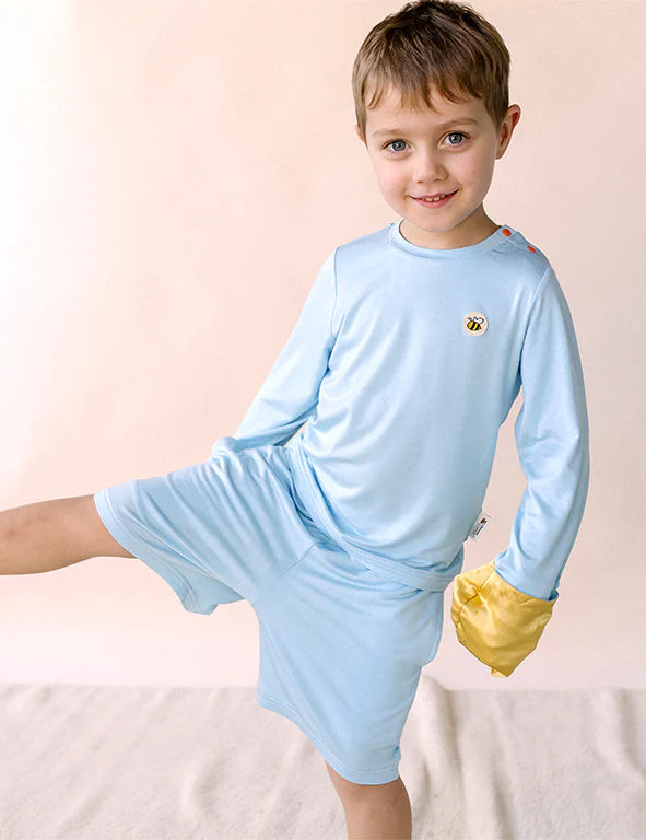 Boy wearing light blue eczema-friendly organic bamboo shorts and long-sleeve top with a gold silk mitten 